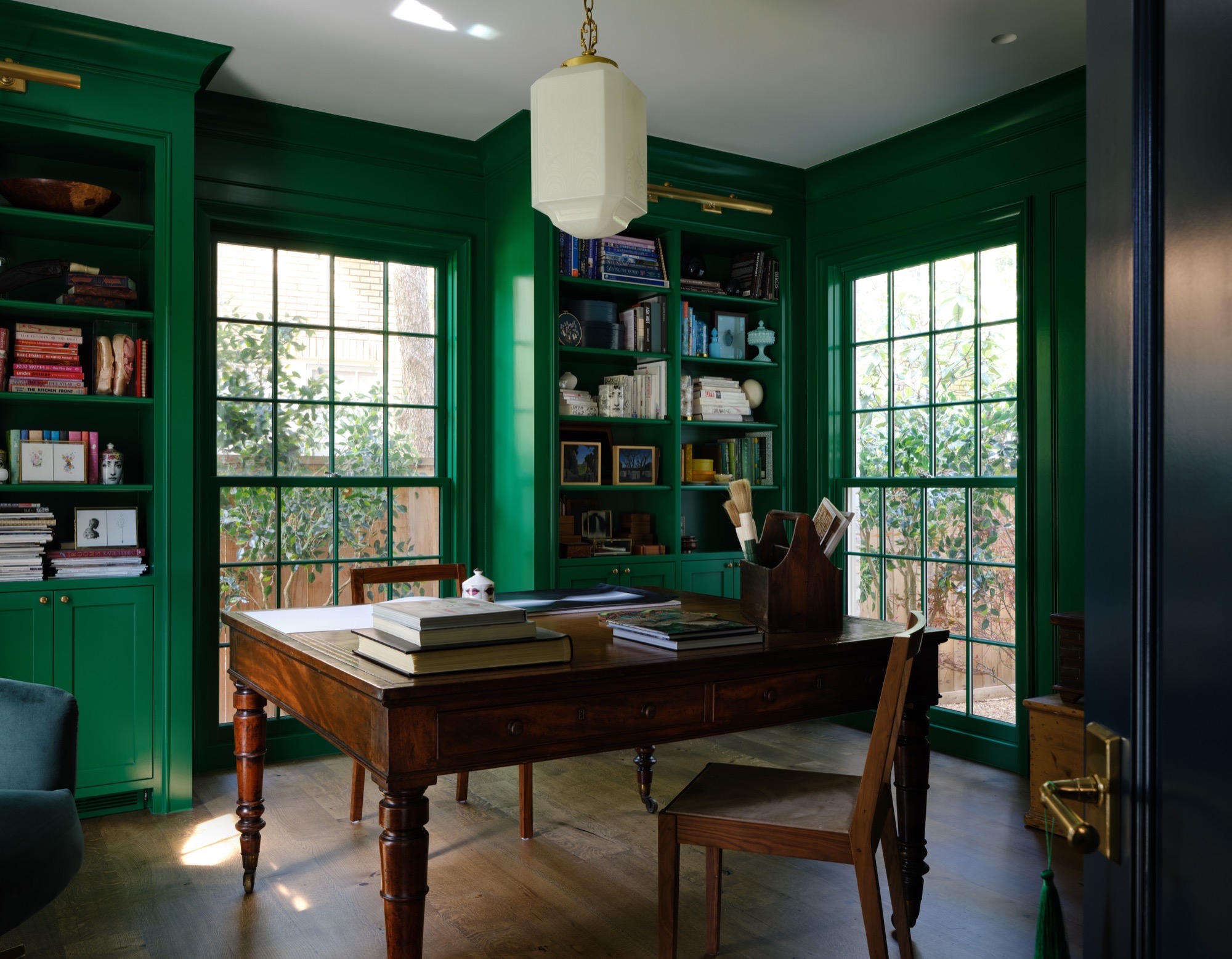 Green home office with built-in bookshelves and divided-light windows in Austin